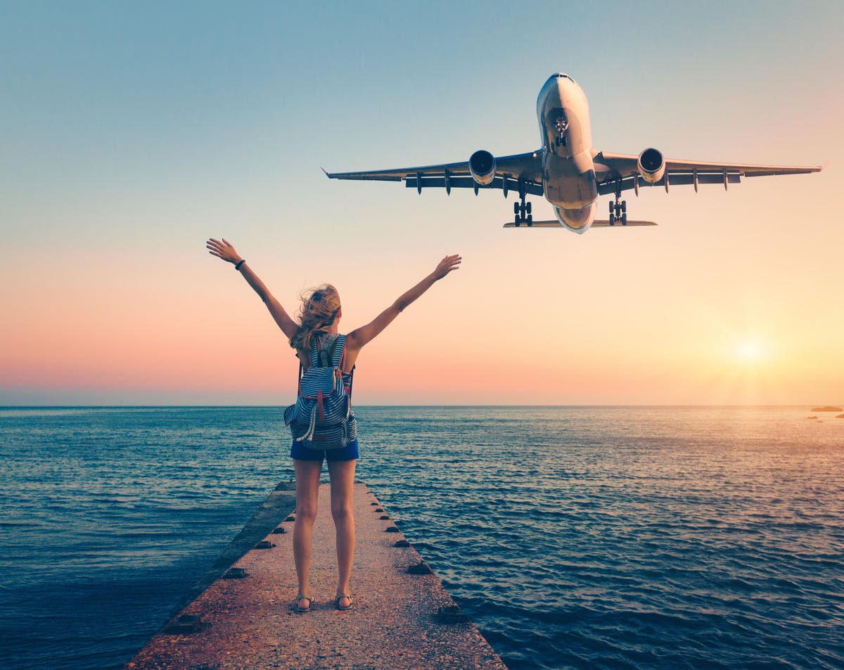 Woman on shoreline, waving at a plane