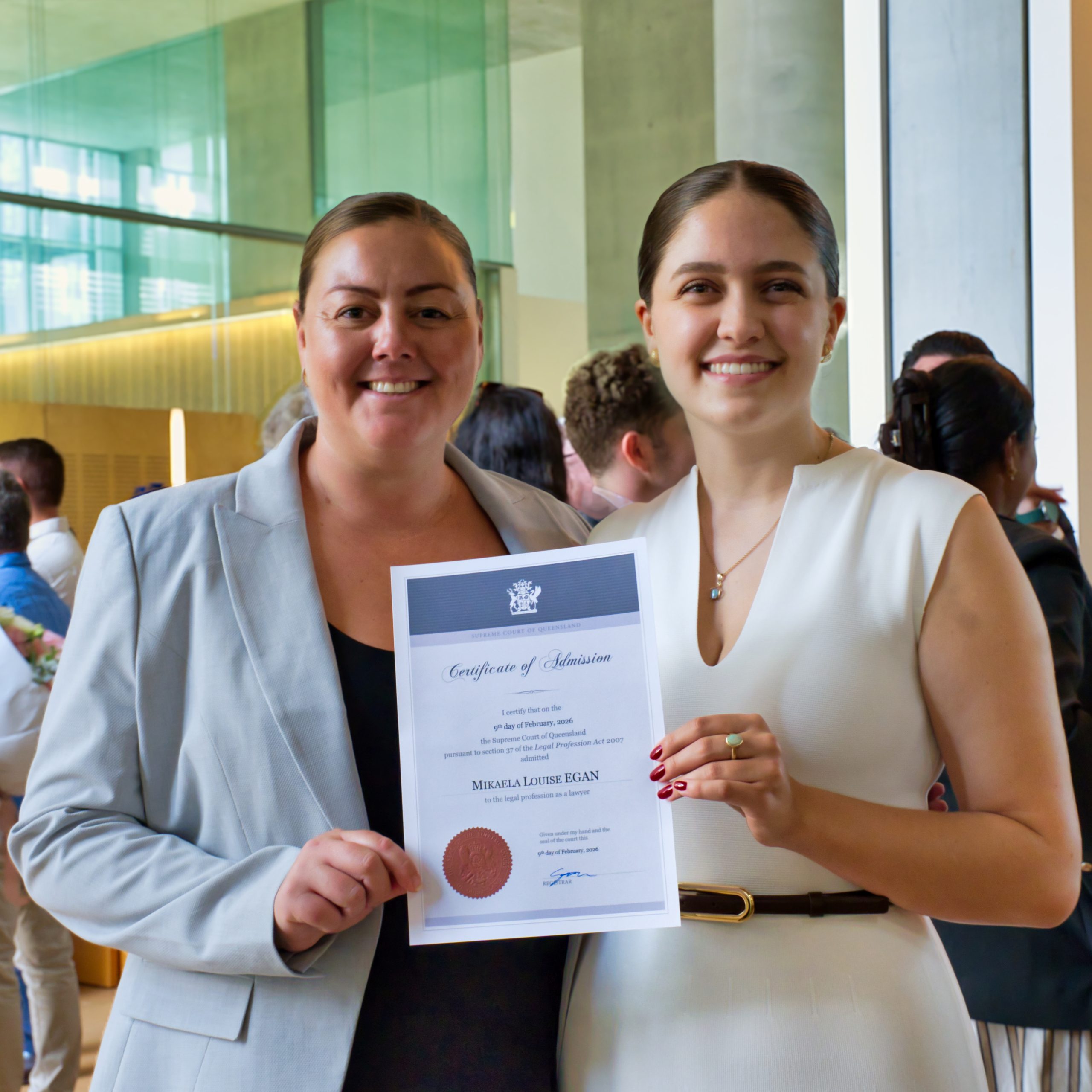 Michelle Wilson (left) and Mikaela Egan (right) stand together inside the Supreme Court of Queensland after the admission ceremony, smiling as Mikaela holds her Certificate of Admission dated 9 February 2026.